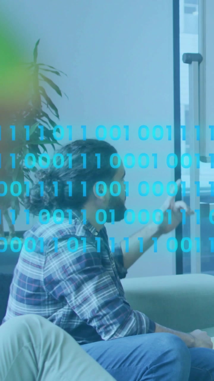 Vertical video: Man on couch noticing binary stream on glass, tapping UI and managing data in tech