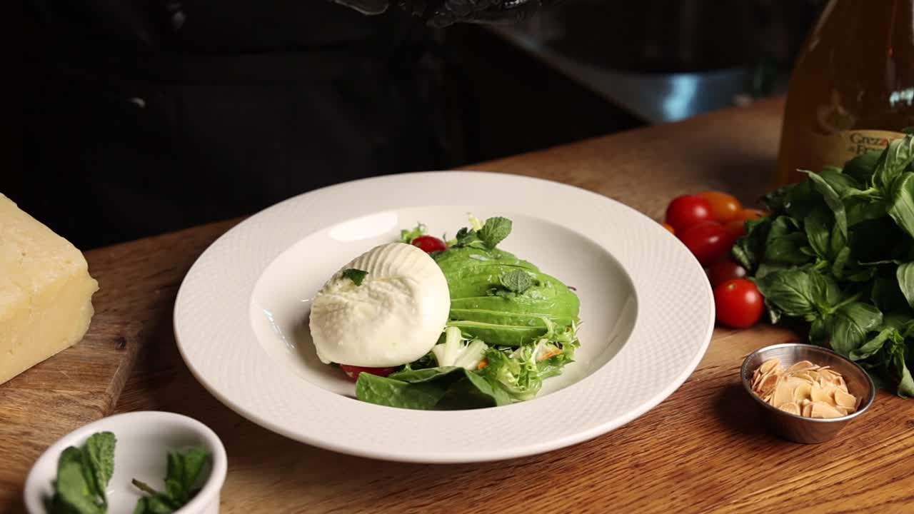 Chef Garnishing Fresh Burrata and Avocado Salad with Mint