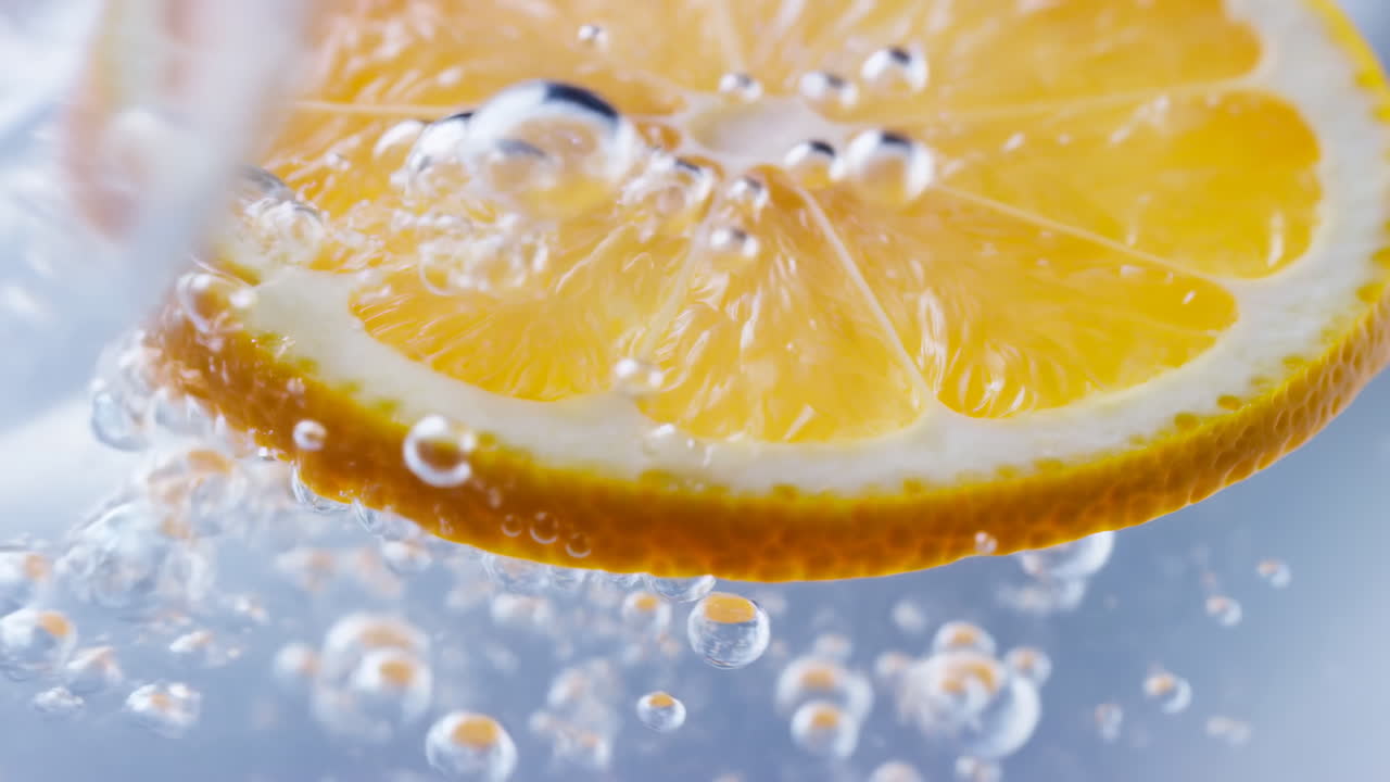 Closeup Orange Slice In Sparkling Water, Bright Citrus Flesh Rimmed With Peel, Surrounded By Rising Bubbles