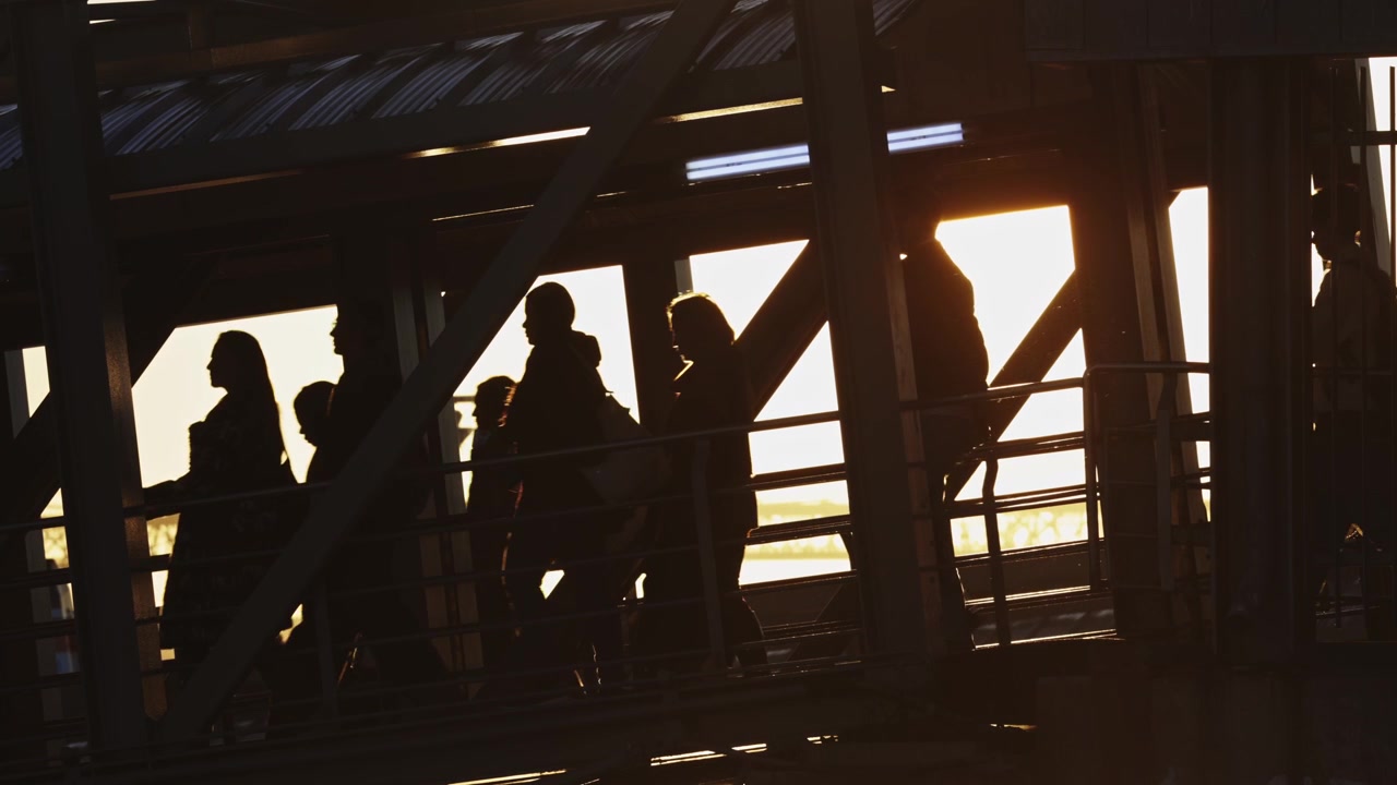 Silhouette di una folla in movimento verso una nave a vapore in fase di imbarco davanti a un sole dorato