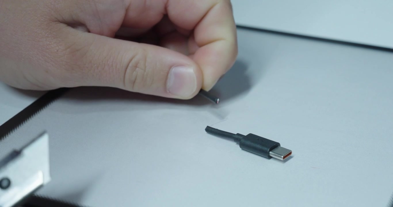 Närbild på en person som klipper en USB-kabel, visar blottade ledningar, modifieringsrisker och elektroniska säkerhetsproblem