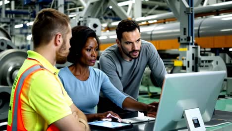 three people are looking at a computer screen in a factory