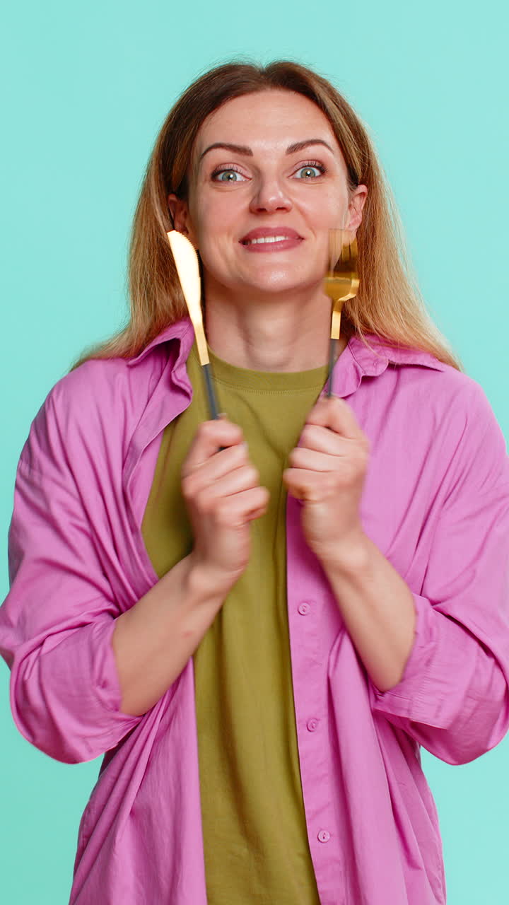 Woman holding fork and knife expressing hunger showing time to eat gesture with eager facial emotion
