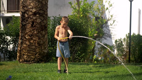 niño tratando de hacer frente al chorro de agua al regar el césped