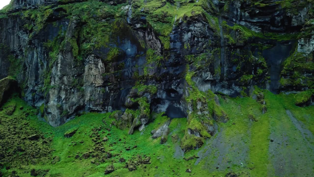 vista aérea del paisaje de un acantilado de montaña oscuro, cubierto de musgo verde, en islandia, con pájaros volando