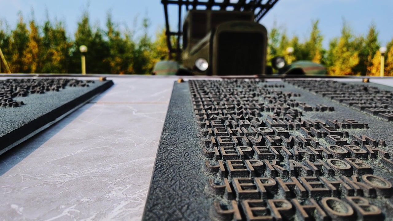 A slow pan reveals engraved text on a stone surface, with a vintage military vehicle and autumn trees visible in the blurred background under a clear sky.
