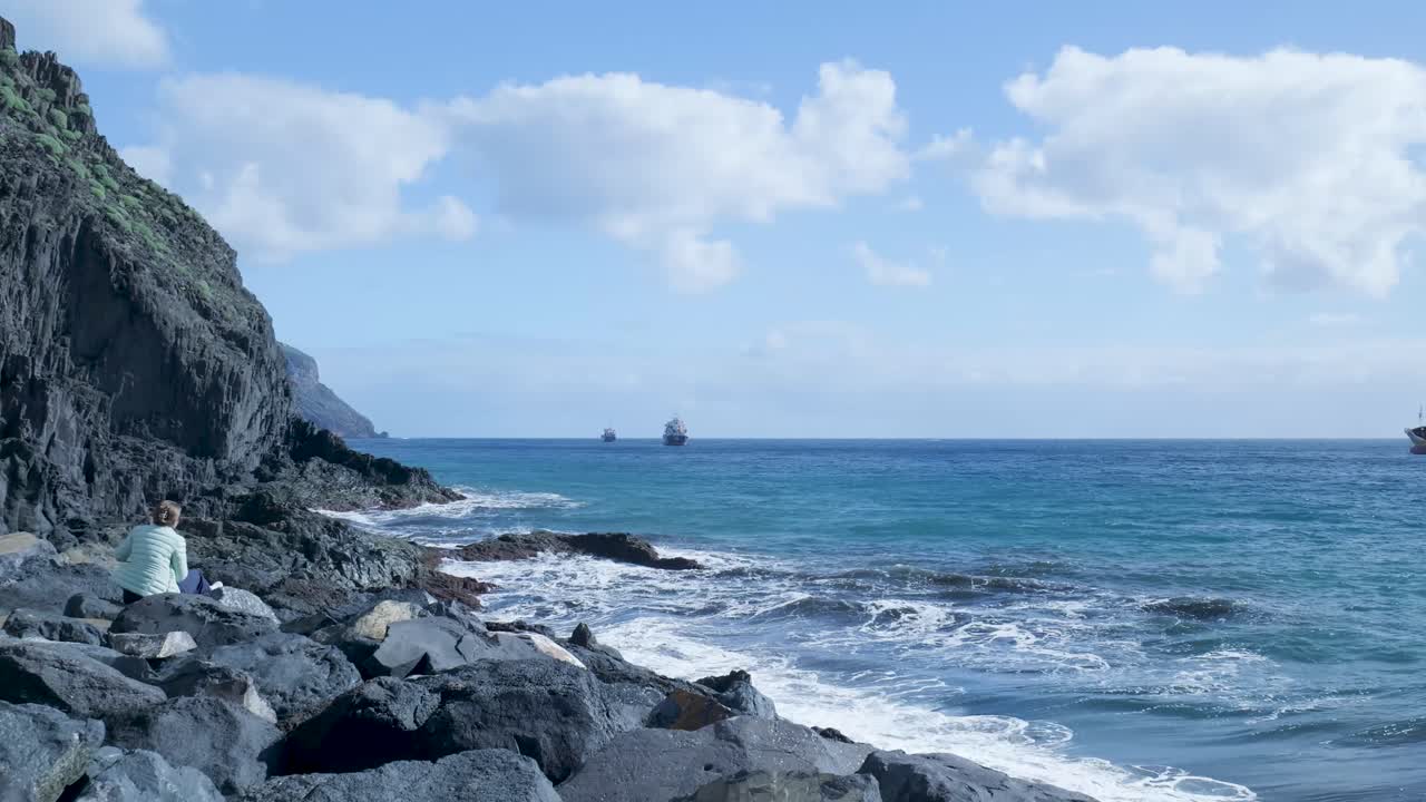 岩場に座り、海の波を見つめる女性