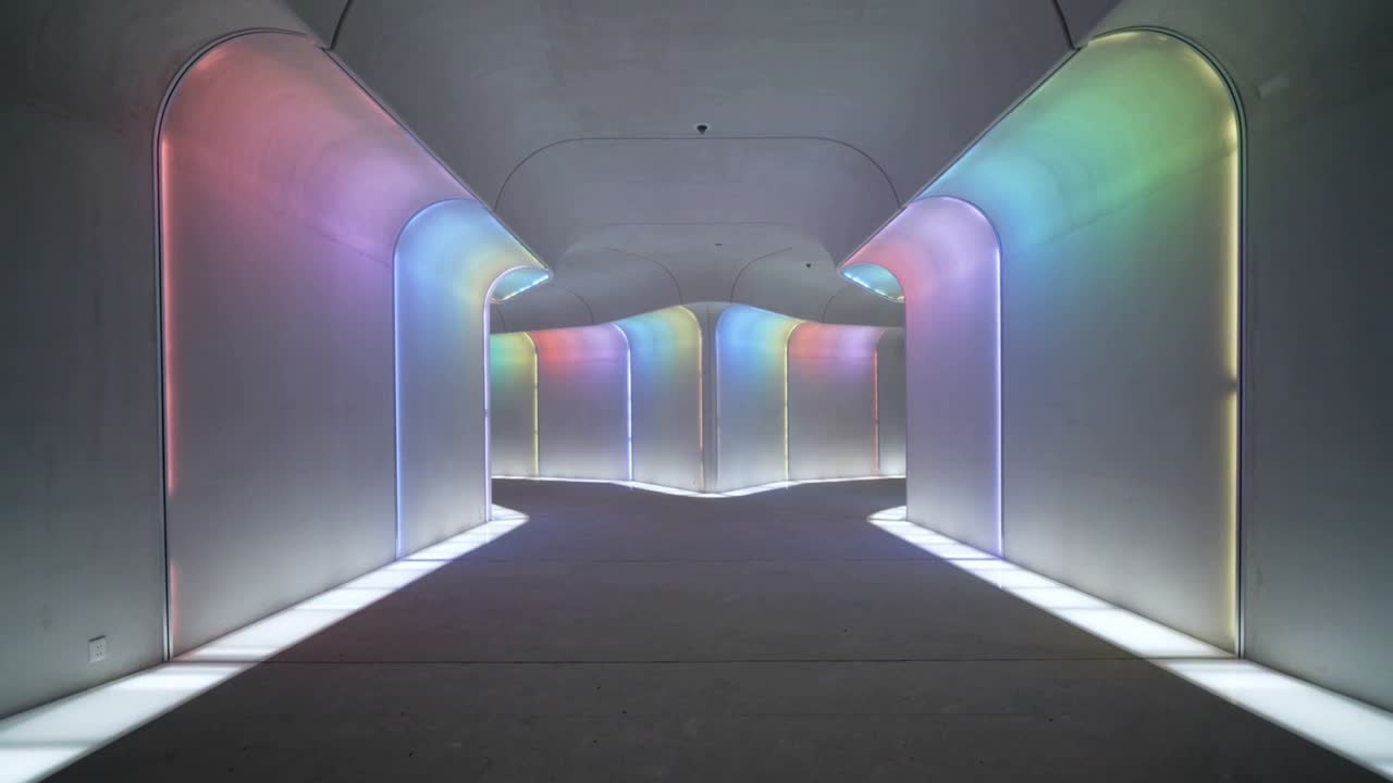 Pulserende RGB LED-strips bader gallerikorridorens paneler og gulvstriber og danner regnbuegradienter.