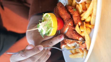 a person eating a breaded cutlet with fries and a lemon tomato garnish