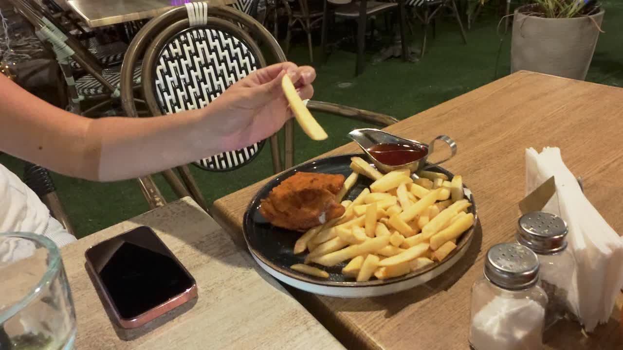 Hand Dipping a French Fry into a Sauce at a Restaurant