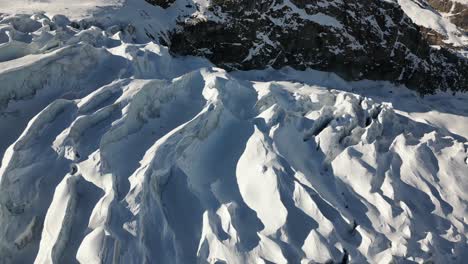 Aerial-pan-shot:-blue-glacier-on-a-Swiss-alps-mountain,-with-its-icy-peaks-and-crevasses