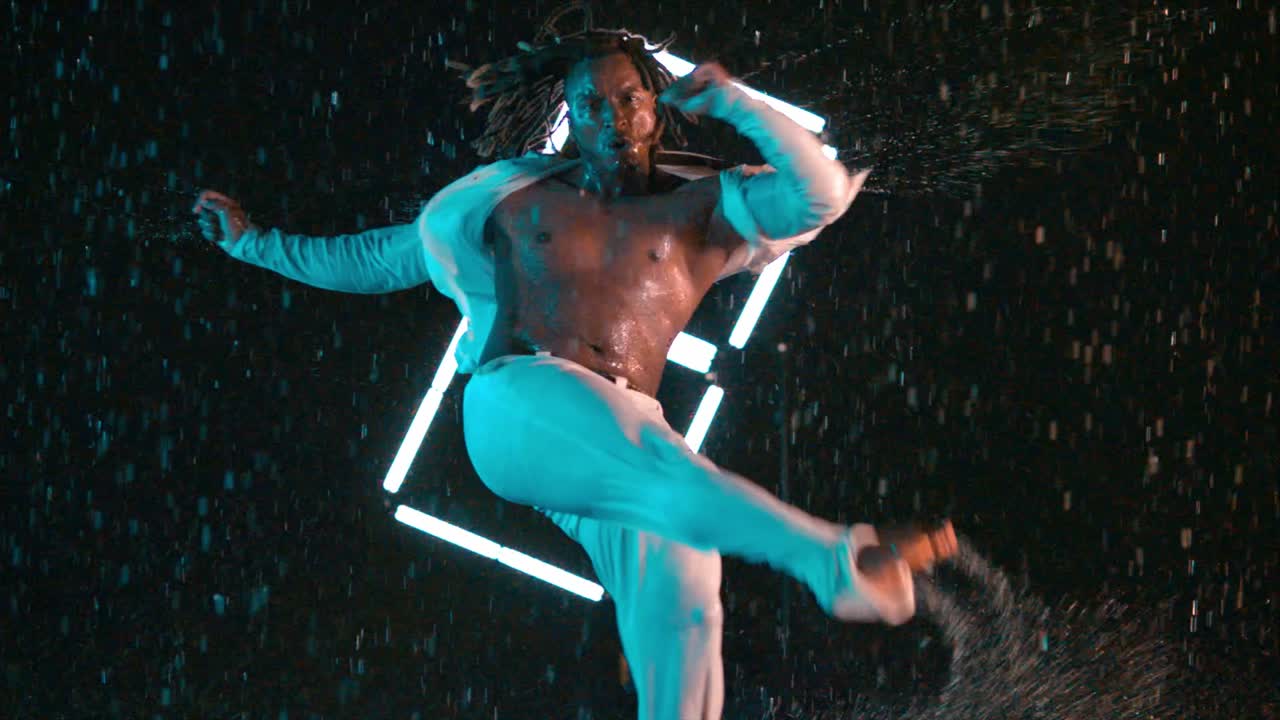 Afroamericano che esegue un calcio di danza Capoeira sotto la pioggia in super slow motion.