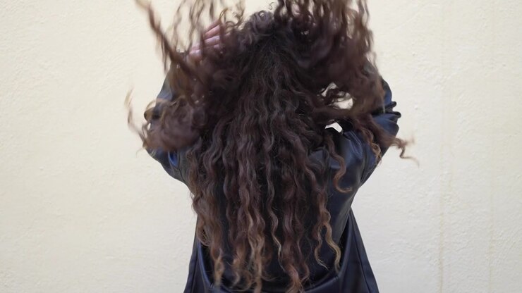 Una mujer con cabello rizado de espaldas a la cámara mostrando sus rasgos.