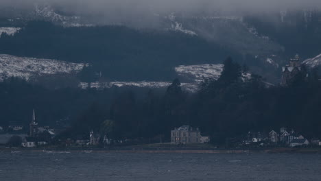 ciudad lejana, casa e iglesia junto al mar con montañas nevadas detrás
