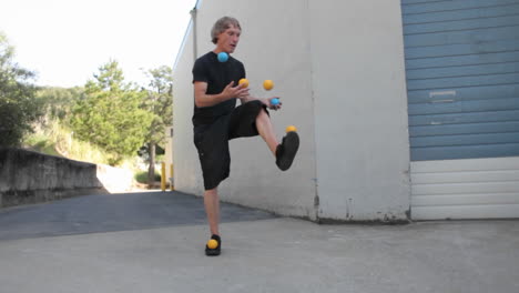 un hombre hace malabarismos con cinco bolas de colores con los pies y las manos