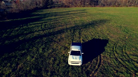 aerial drone tracking scene of white silverado pickup truck driving on green grassy lawn of rural area in indianapolis