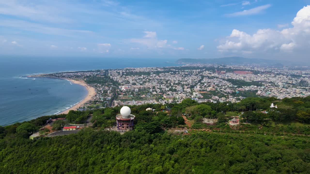 Aerial drone shot of Vizag city at sunset, with the golden glow reflecting on the city’s buildings and the nearby ocean.