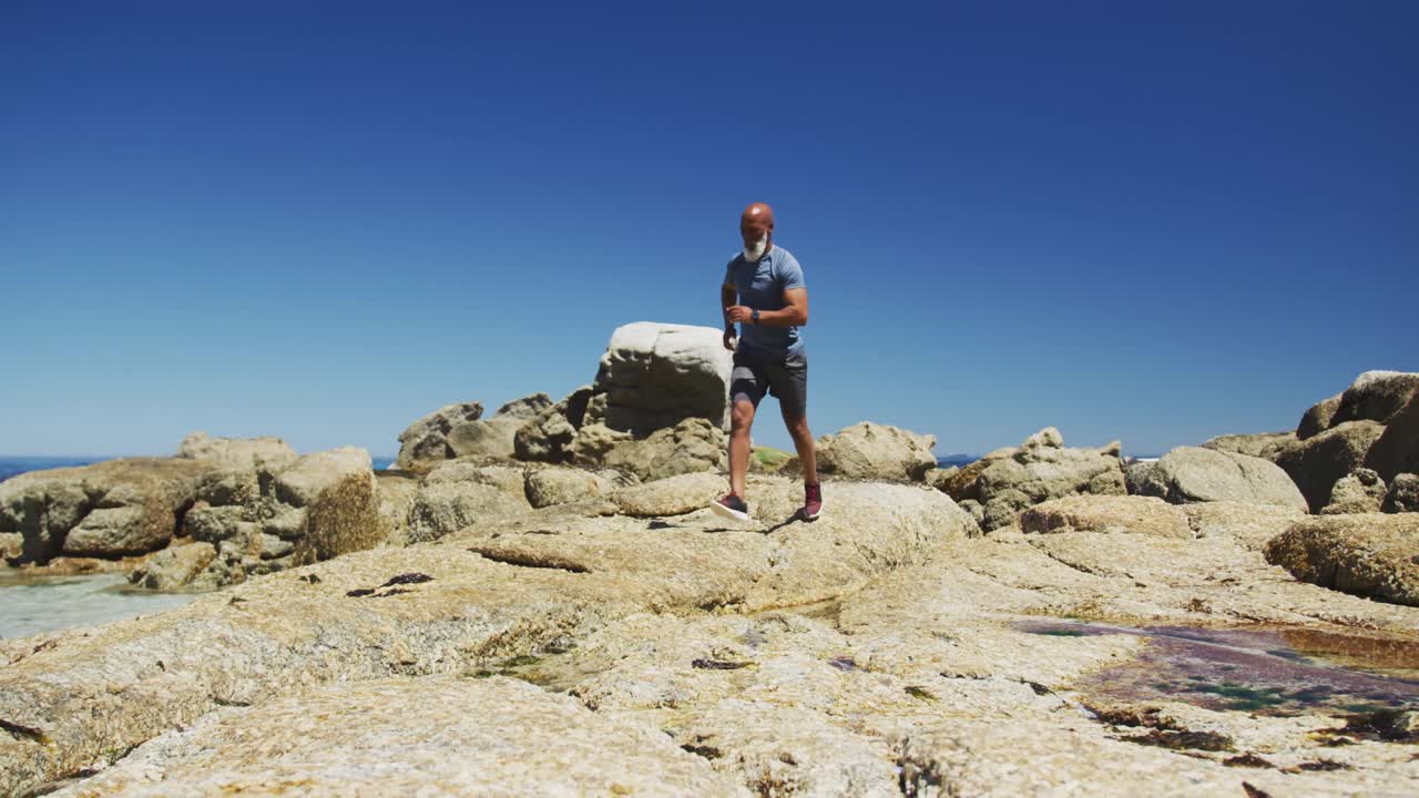 시니어 아프리카계 미국인 남자가 바 ⁇ 가의 바위 위에서 달리기를 연습하고 있습니다.