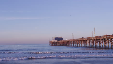 ocean waves at shoreline of beach with fishing pier at dawn in newport beach, california, usa