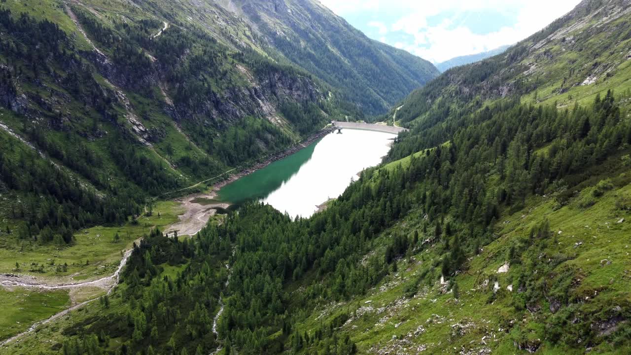 Enorme lago artificiale in una valle circondato da scogliere e alberi nelle Alpi in Carinzia, Austria