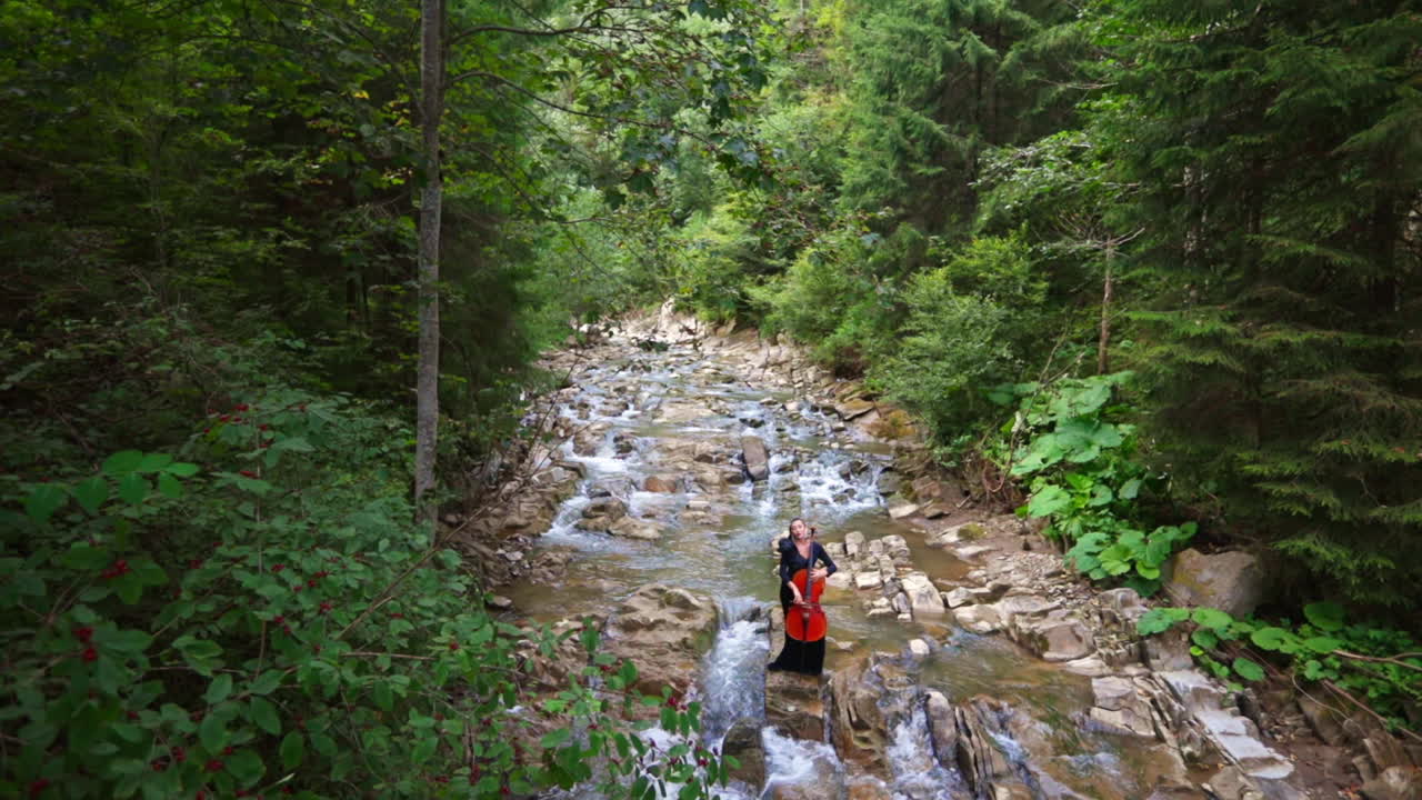 Cellist playing on instrument outdoors. Female musician performs on cello at mountains outdoor