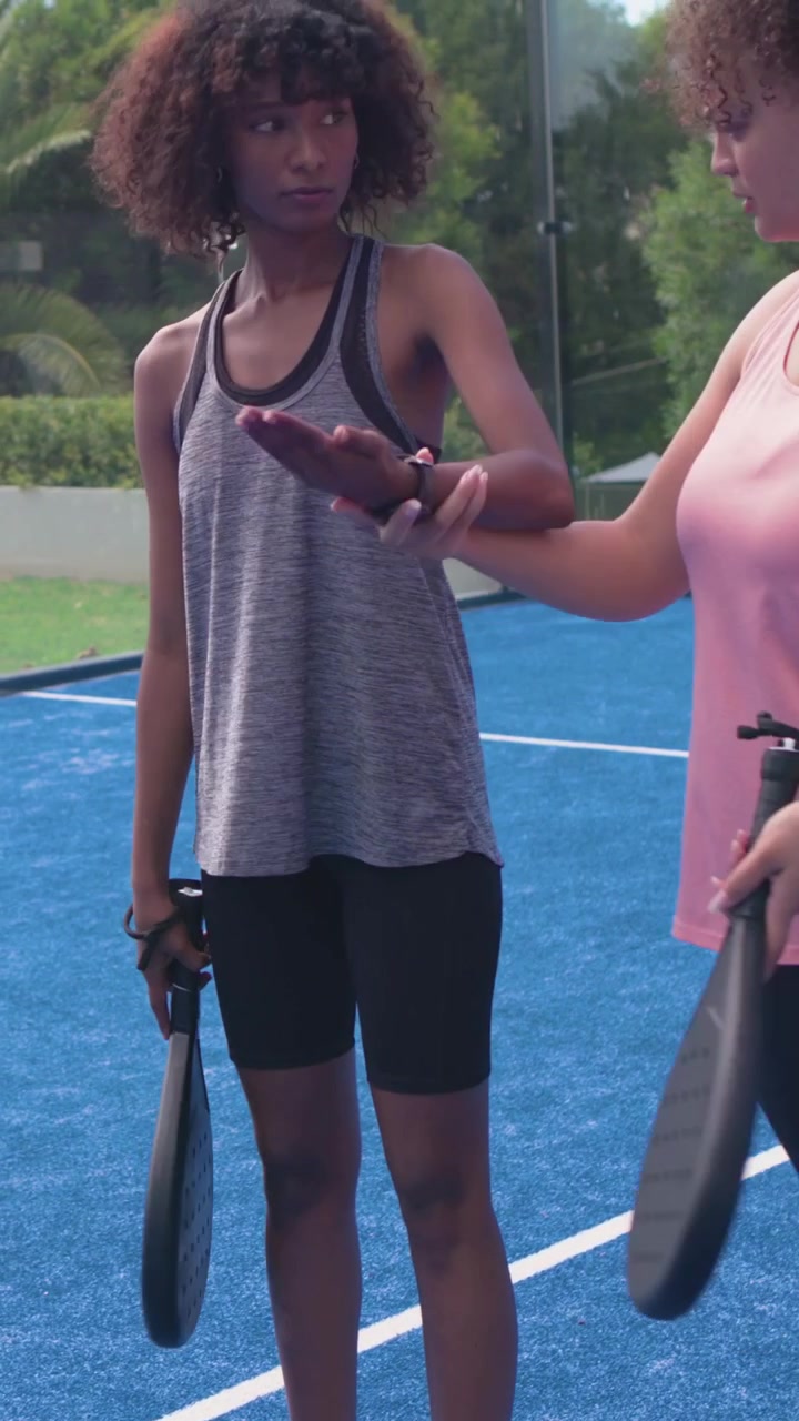 Vídeo vertical: Apertando as mãos, mulher de regata cinza com raquete praticando forehand para aprender em quadra azul.