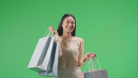 An Asian Shopping Woman With Shopping Bags Smile To Camera While Standing In Front Of Green Screen