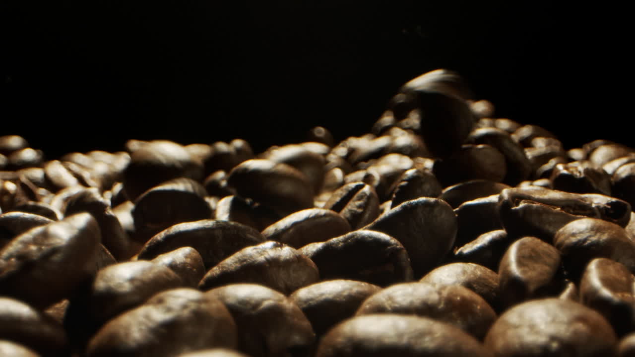 Close Camera movement through falling fresh coffee beans into a pile of beans laying on a wooden surface