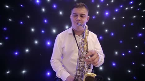 tilt up shot of biracial jazz musician in checkered suit and bowtie playing saxophone while sitting against black band member in dimly lit bar, rehearsing and checking sound before live performance