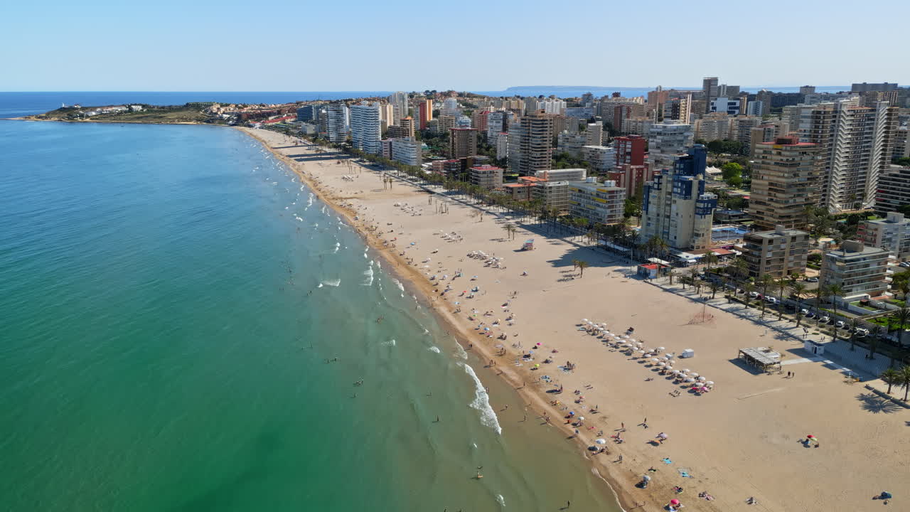 Aerial drone view of the buildings along the coastline with people relaxing on the beach in Benidorm, Spain in daylight