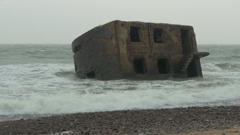 big stormy waves breaking against abandoned seaside fortification building ruins at karosta northern forts in liepaja, baltic sea coastline, wave splash, rainy overcast day, medium shot