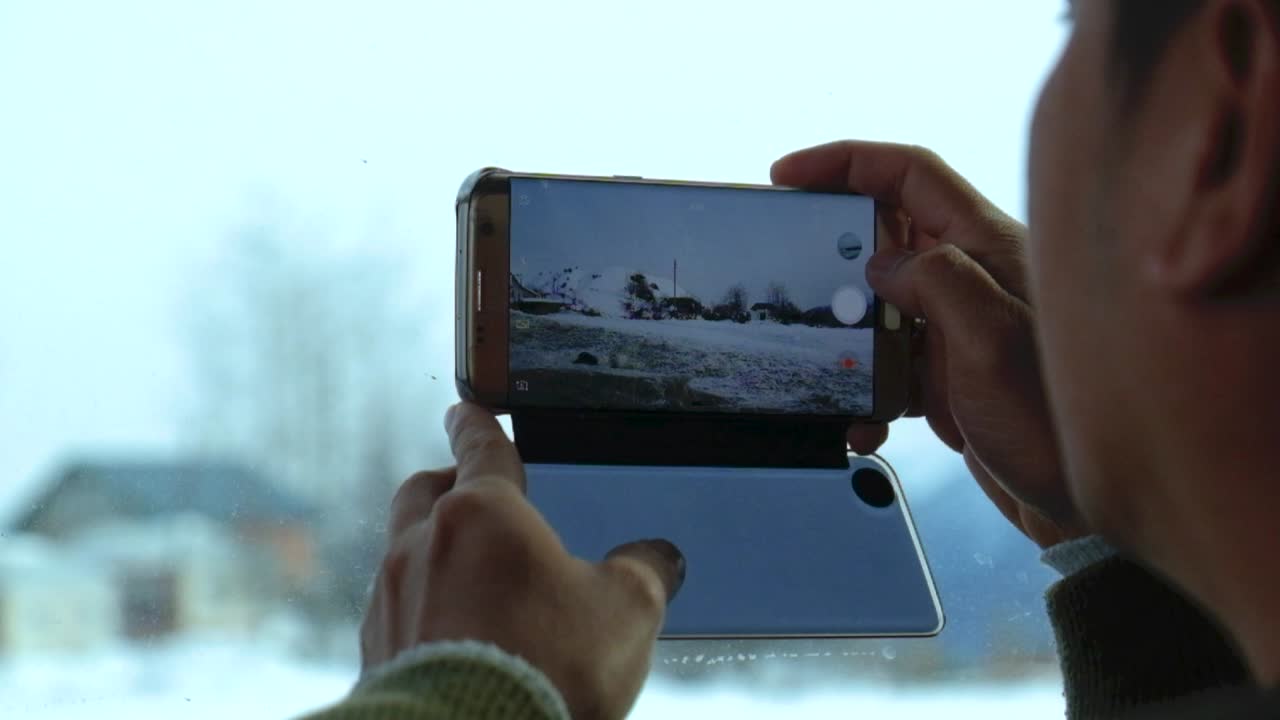 Adult male using a Galaxy S7 Edge to record snow landscape from a moving vehicle