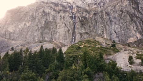 Aerial-approaching-a-distant,-very-high-mountain-waterfall-flying-over-a-forest-in-Tzoumerka,-Greece