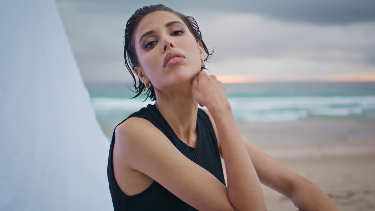 Primo piano di una donna affascinante in posa sulla costa. Modella di moda che posa su una sedia a sdraio in riva all'oceano.