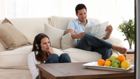 Man-reading-the-newspaper-while-a-woman-listens-to-music