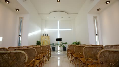 moving-shot-of-the-interior-of-a-small-chapel-with-wooden-chairs-where-sunlight-enters-through-a-cross-on-the-wall