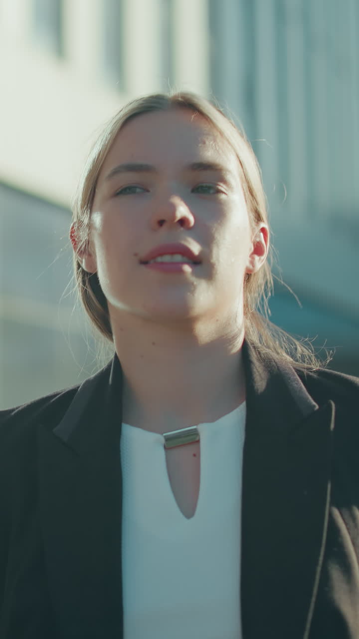 Close up of banker in black suit holding file folder and coffee cup while walking along path with blurred background of parked cars and urban buildings during bright morning commute to office