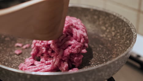 using the spoon to move the uncooked red ground beef into the pan as it cooks over the stove - close up view in slow motion