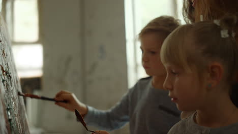 female painter teaching children in studio. boy and girl painting indoors.