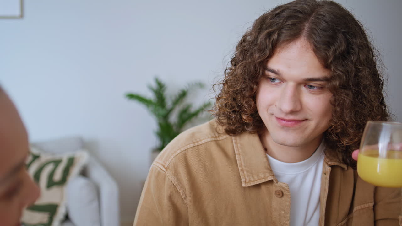Relaxed boyfriend drinking juice talking to happy girlfriend at kitchen closeup