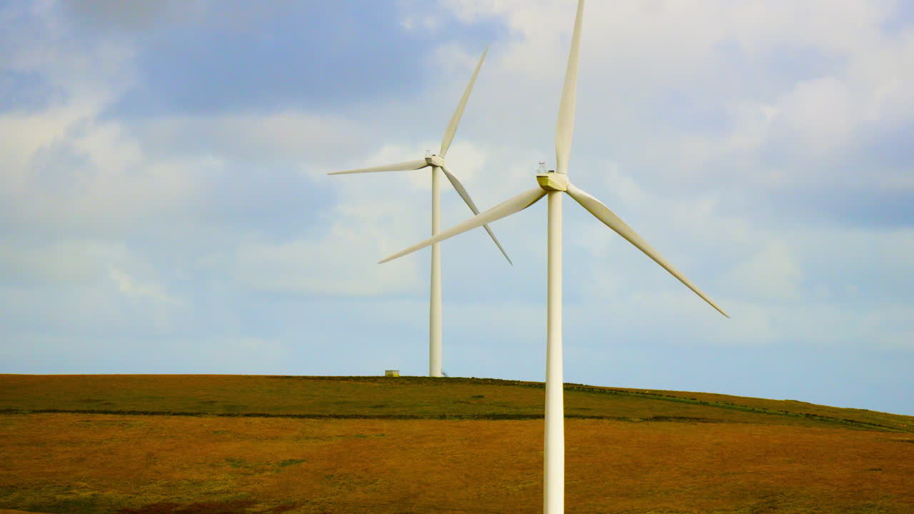 Two Wind Turbines Spinning in Fast Windy Environment on Wild Grass Covered Hill and Blue Sky Background. Clean Renewable Energy Generated