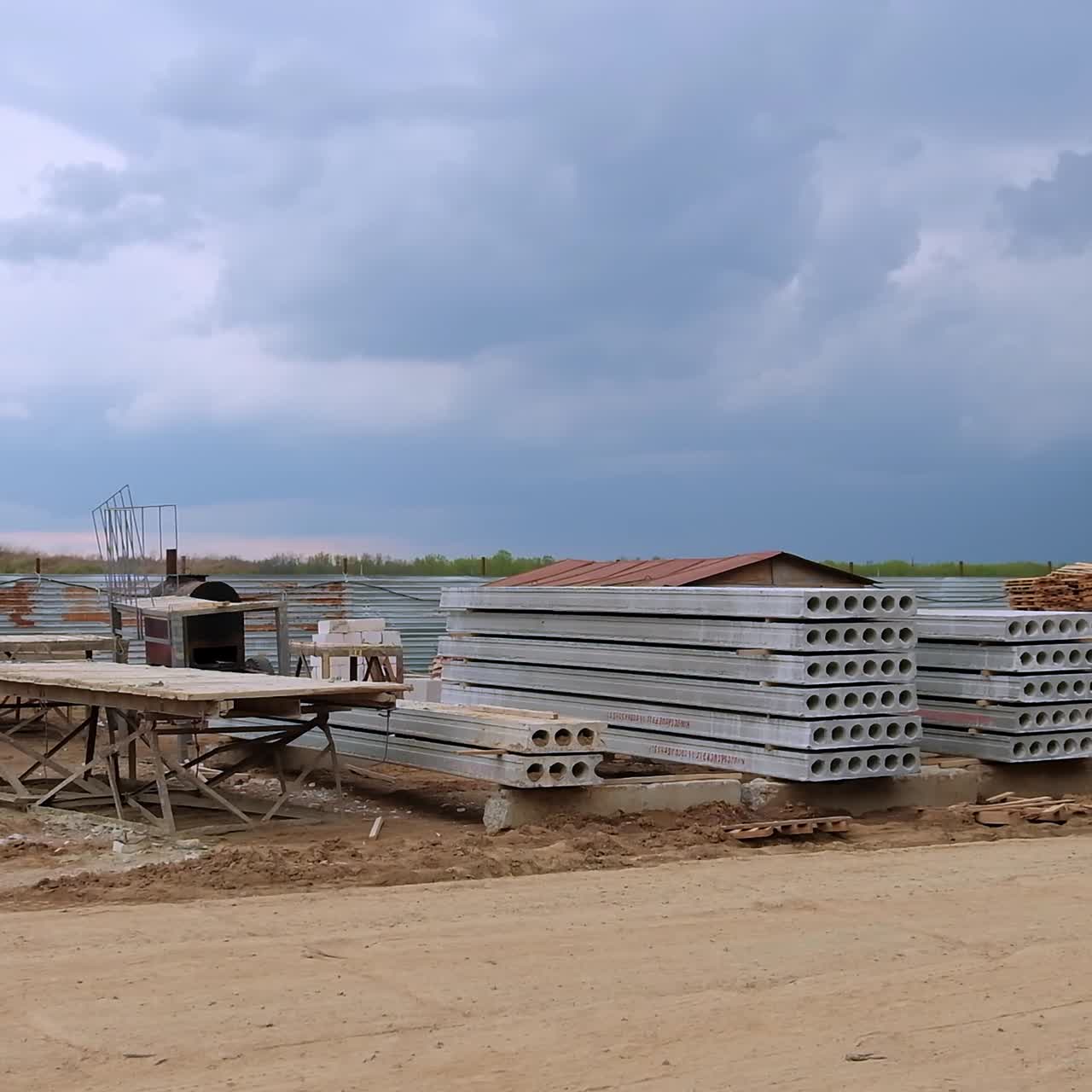 Construction site outdoors with materials for building surrounded by the metal fence. Grey cloudy sky at backdrop