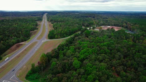 Motorway-in-the-middle-of-nature-very-saturated-vivid-pop-colours-trees-surrounding-side-way-to-a-building-demolished-site-cars-passing-by-traveling-birds-view-transportation-in-forest-Brent-Alabama