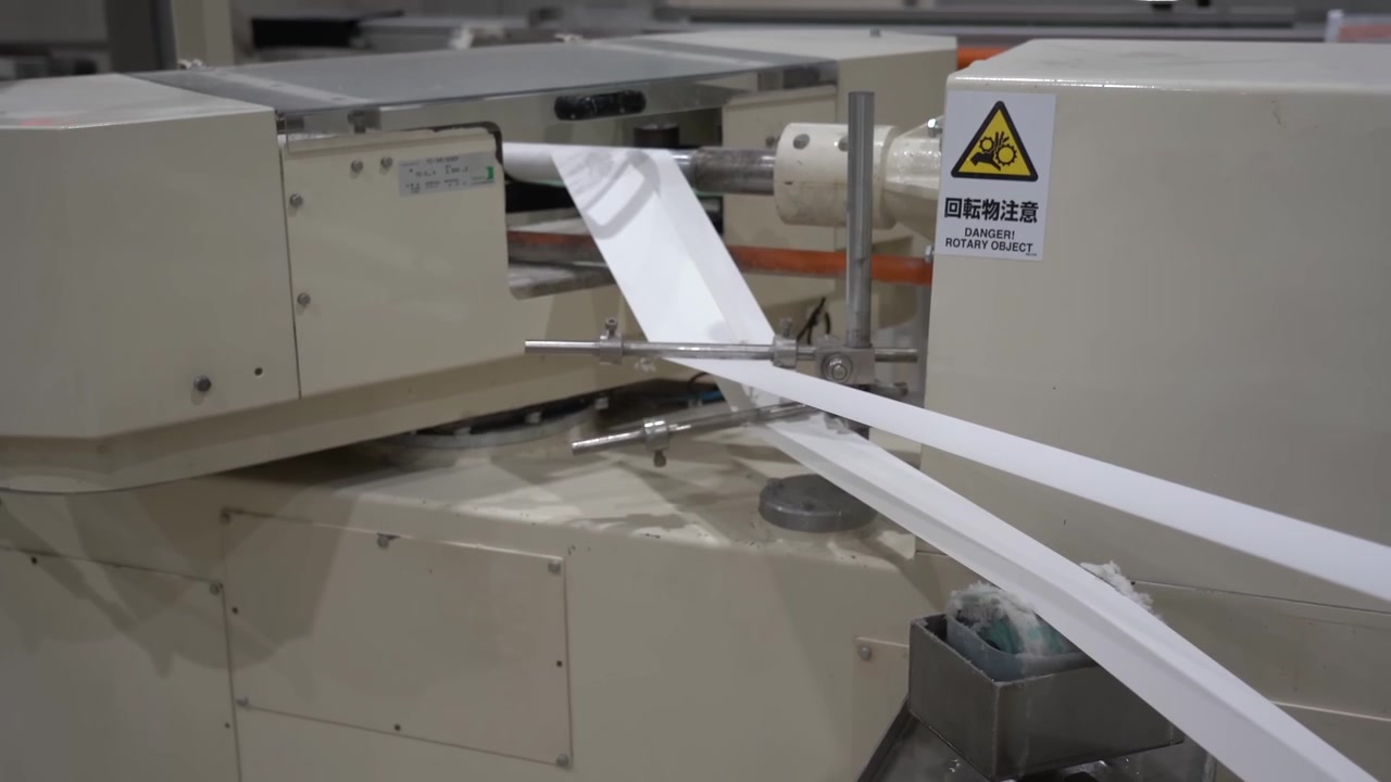 製紙工場で加工機械の中を流れていく白いティッシュペーパーの連続した帯。