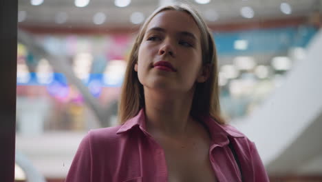 dama en vestido rosa sin botones se relaja con una suave sonrisa en su cara mientras el ascensor sube, el fondo presenta elementos borrosos y luces bokeh coloridas, vistas a través del vidrio
