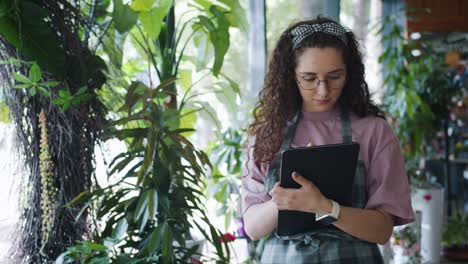 good-looking flower shop owner counting plants and using tablet at work