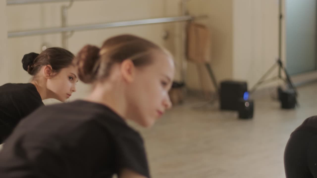 группа молодых студентов балета в черной танцевальной одежде практикует позиции в просторной балетной студии с деревянным полом и настенными решетками. сосредоточенные выражения и синхронизированные движения.