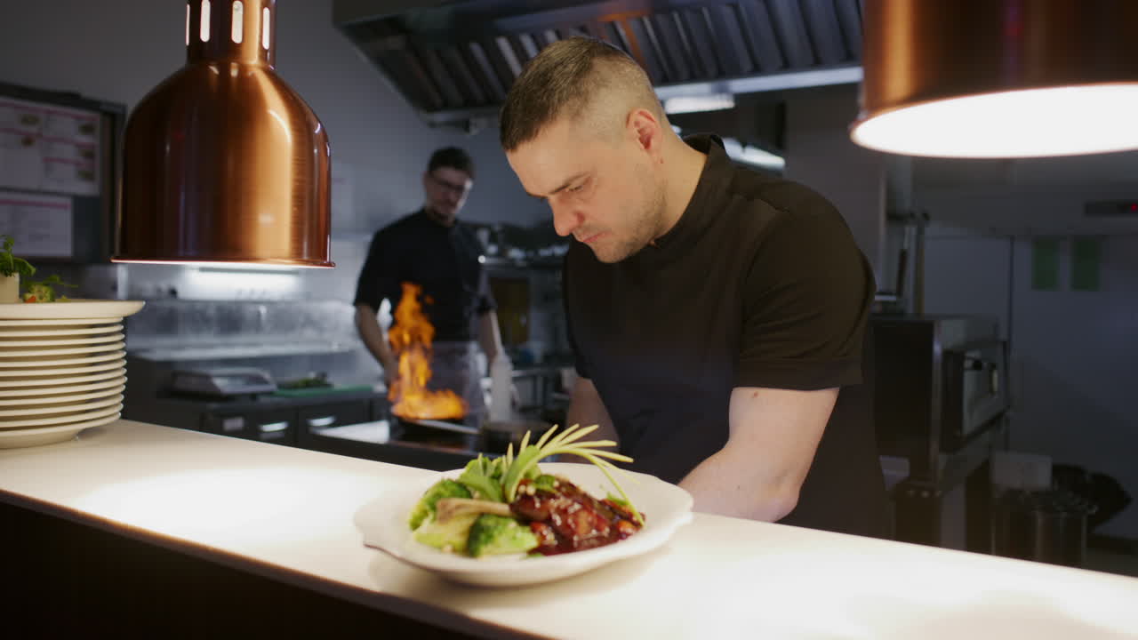 Chef che usa le pinzette per guarnire un piatto gourmet con un'erba aromatica in cucina