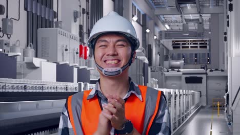 close up of asian male engineer with safety helmet smiling and clapping his hands while standing at pharmaceutical factory, vaccine production facility