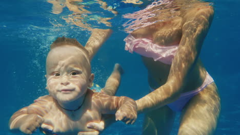 the baby boy dives in the pool underwater video mum carefully supports him